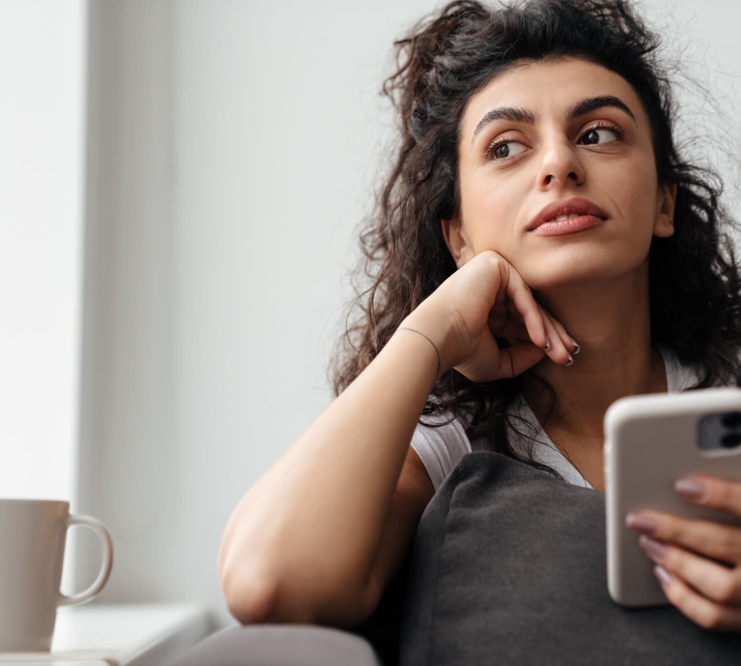 A woman at home, phone in hand, lost in thought